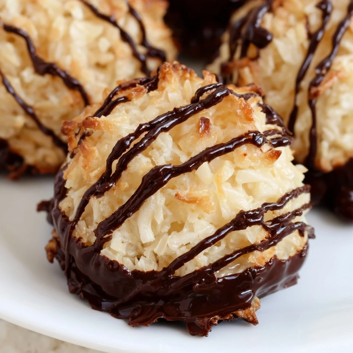 Freshly baked Coconut Macaroons stacked on a wire rack, featuring rich chocolate drizzle and a sweet, toasty coconut aroma.