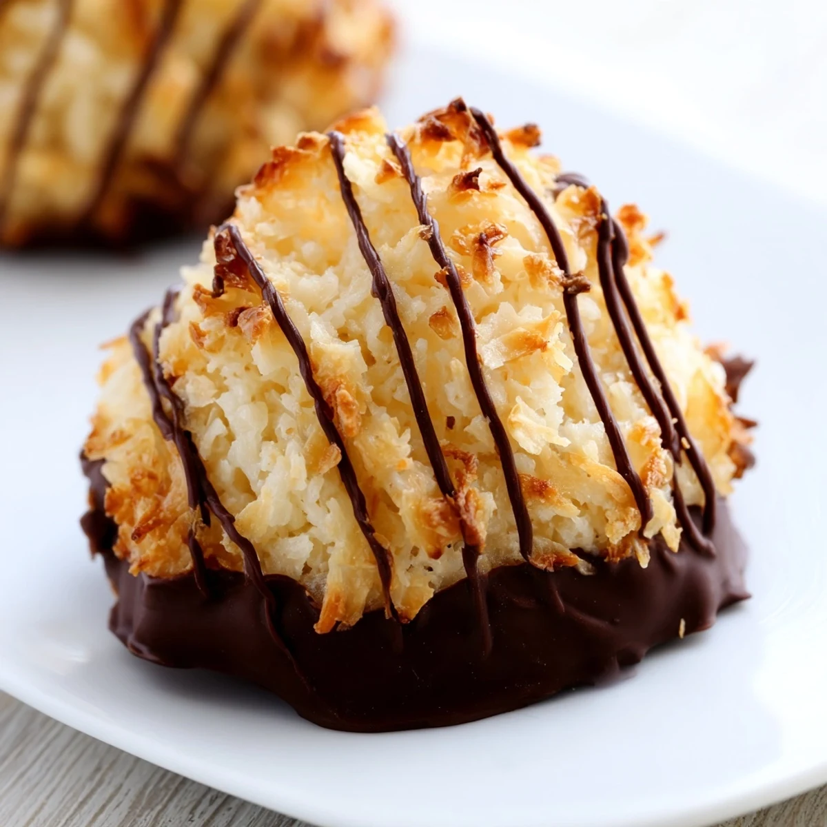 Gluten-free Coconut Macaroons with chocolate drizzle, arranged on parchment paper with a bowl of shredded coconut nearby.