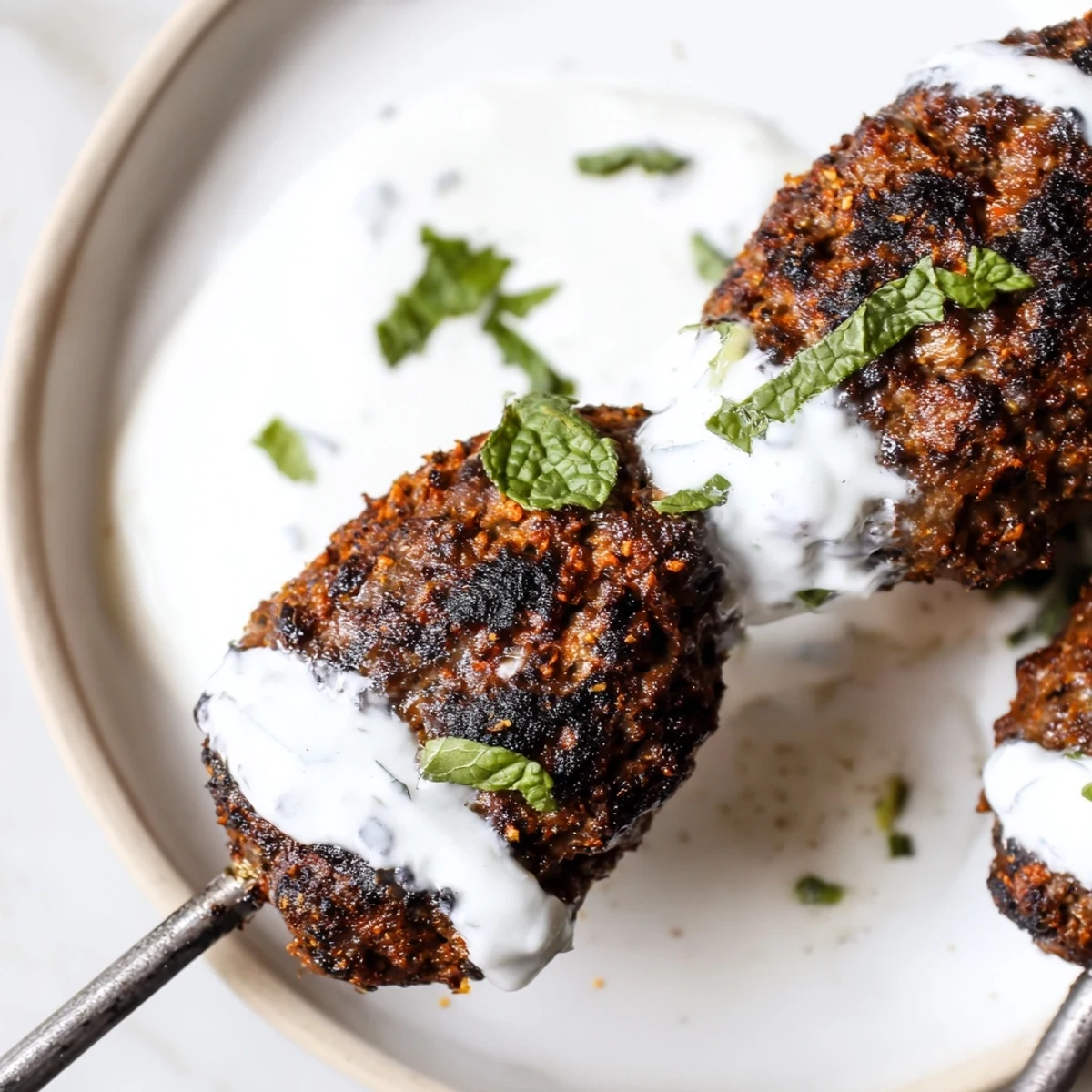 Grilled Beef Kofta Kebabs with Tzatziki Sauce are sizzling on the grill with visible char marks.