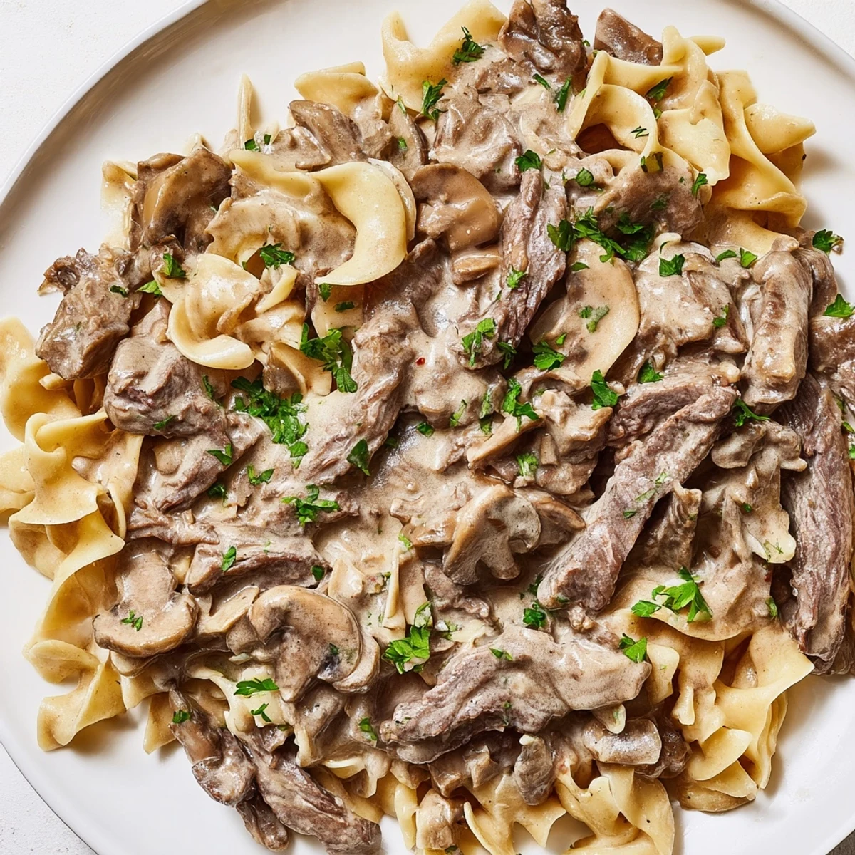 Creamy beef stroganoff served over buttery egg noodles, garnished with fresh parsley.