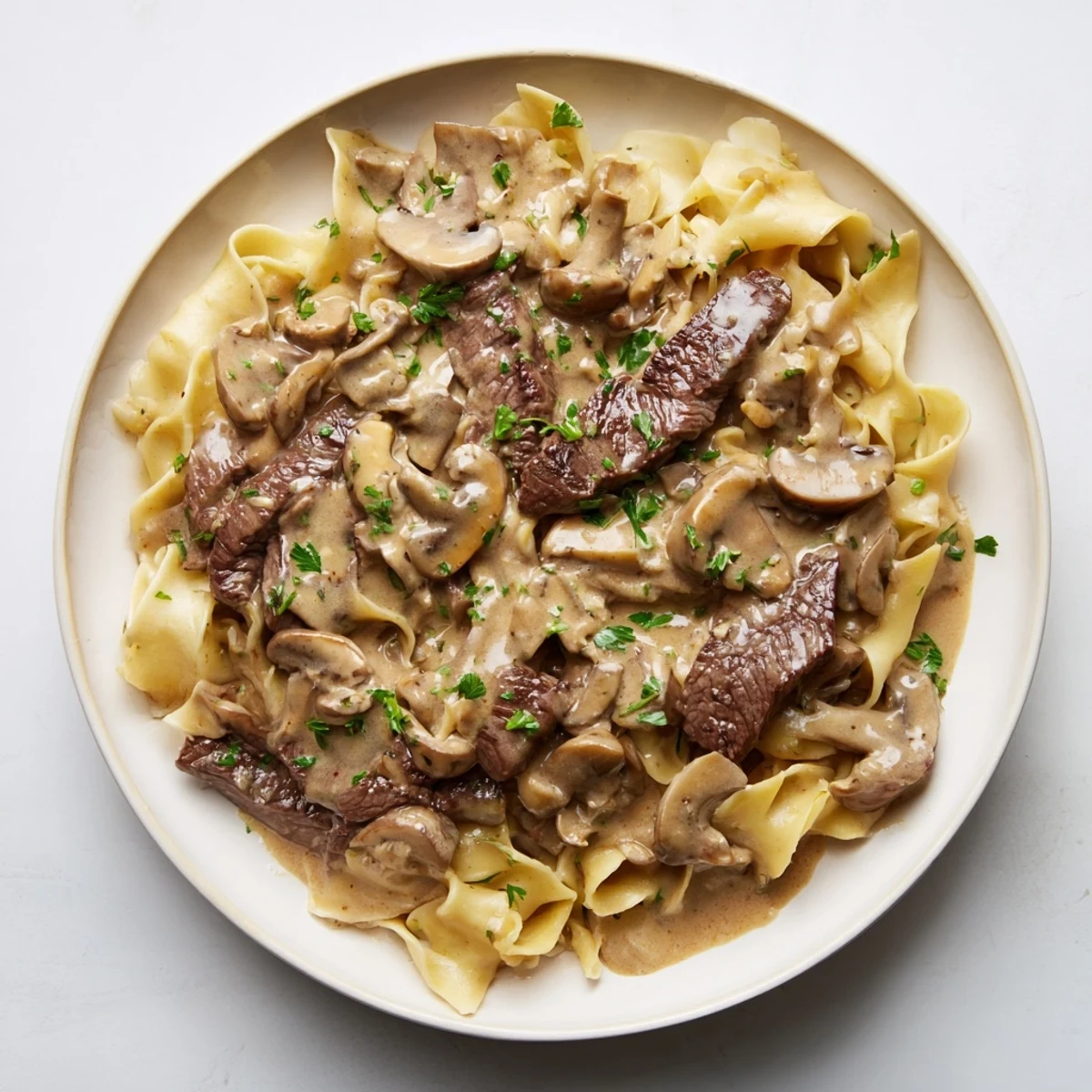 Beef Stroganoff over Egg Noodles with creamy mushroom sauce and tender beef strips, garnished with fresh parsley.