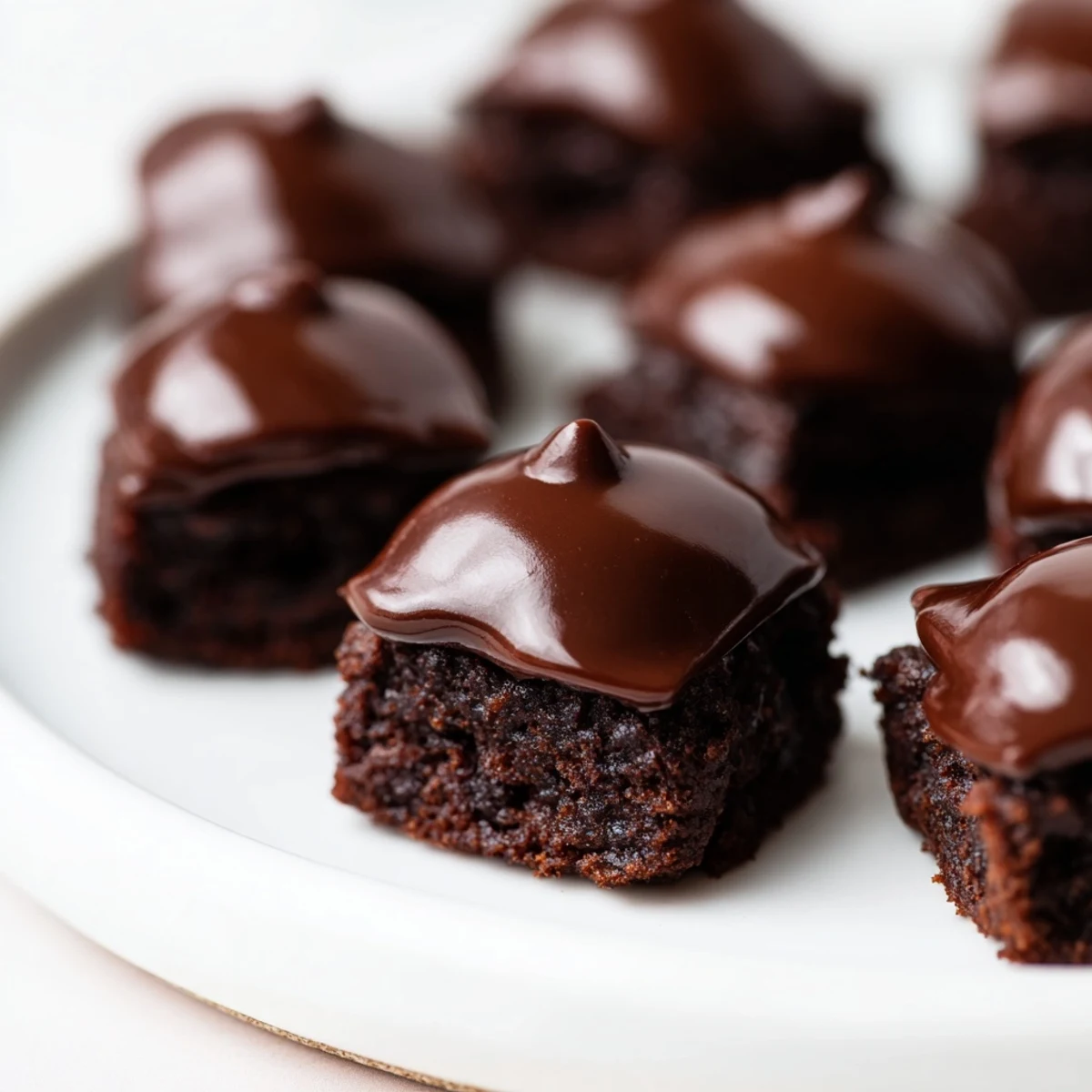A close-up view of Mint Brownie Bites with Ganache, showing fudgy mini brownies topped with glossy chocolate and fresh mint leaves.  