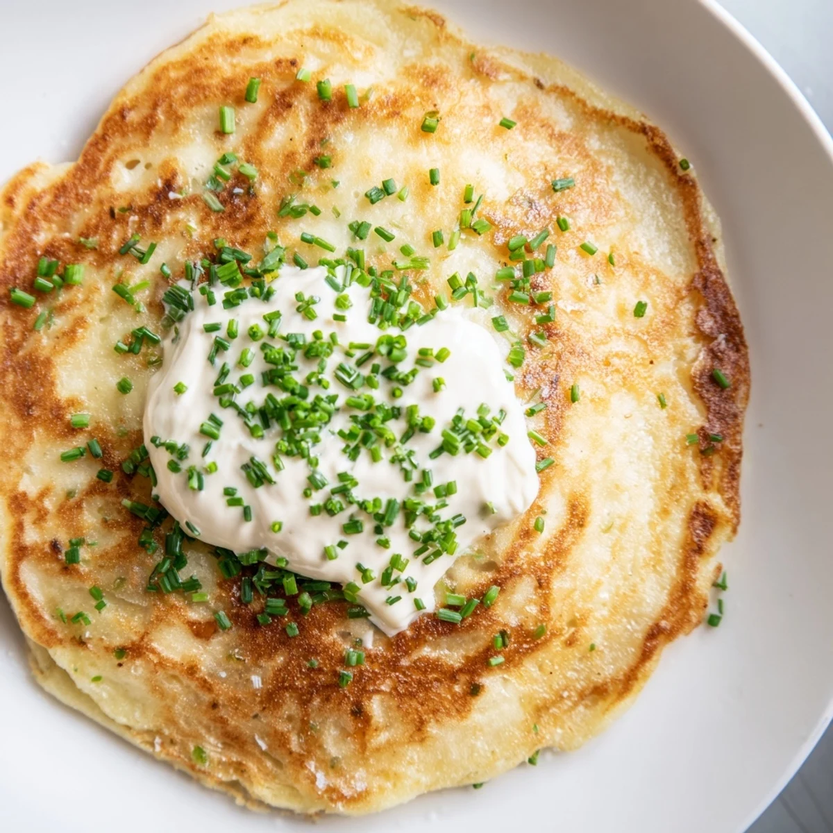 Crispy Irish Boxty with Sour Cream topped with fresh chives on a rustic plate, ready to serve as a hearty breakfast or side.  