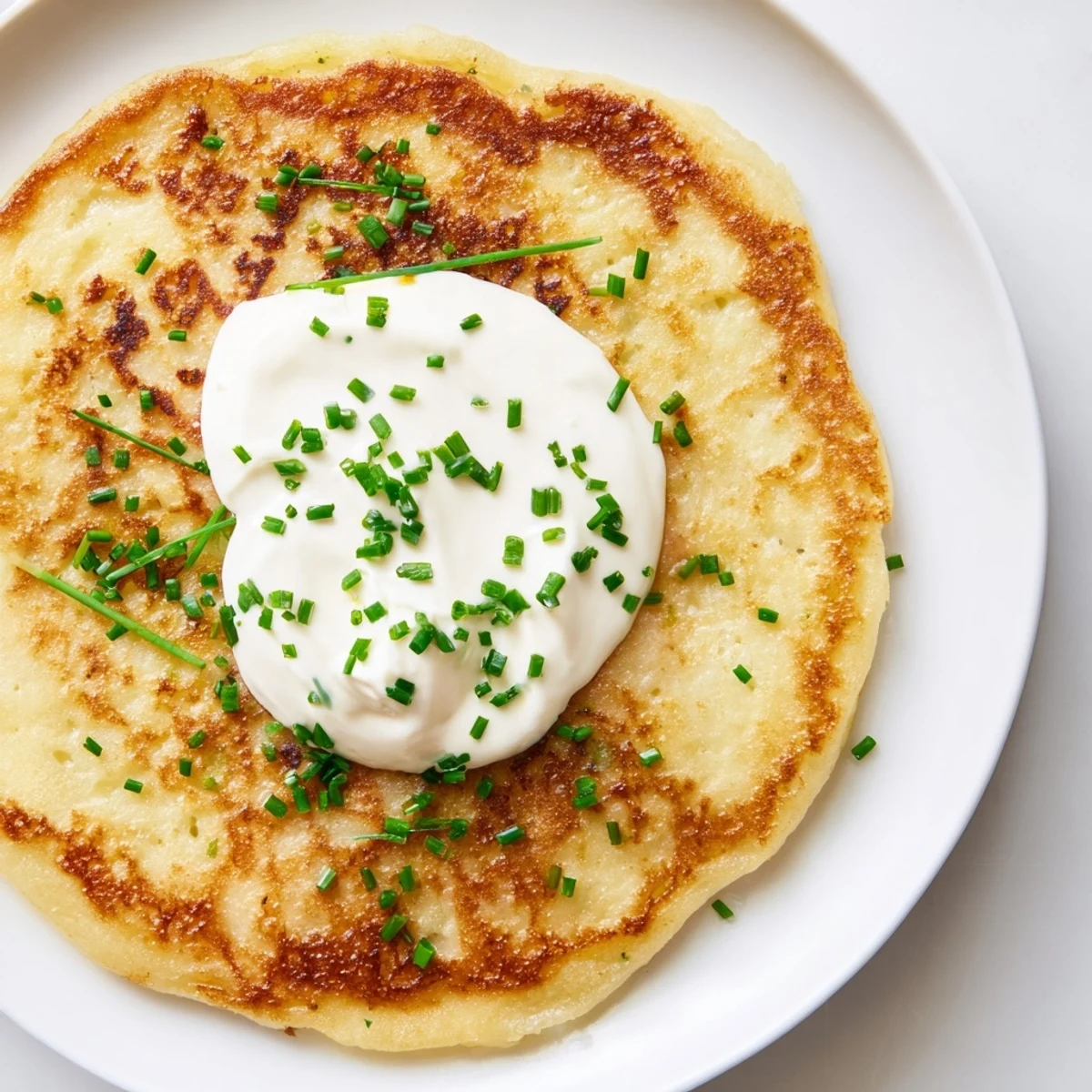 Warm Irish Boxty pancakes served from a skillet, garnished with a dollop of sour cream and fresh chives for a classic touch.
