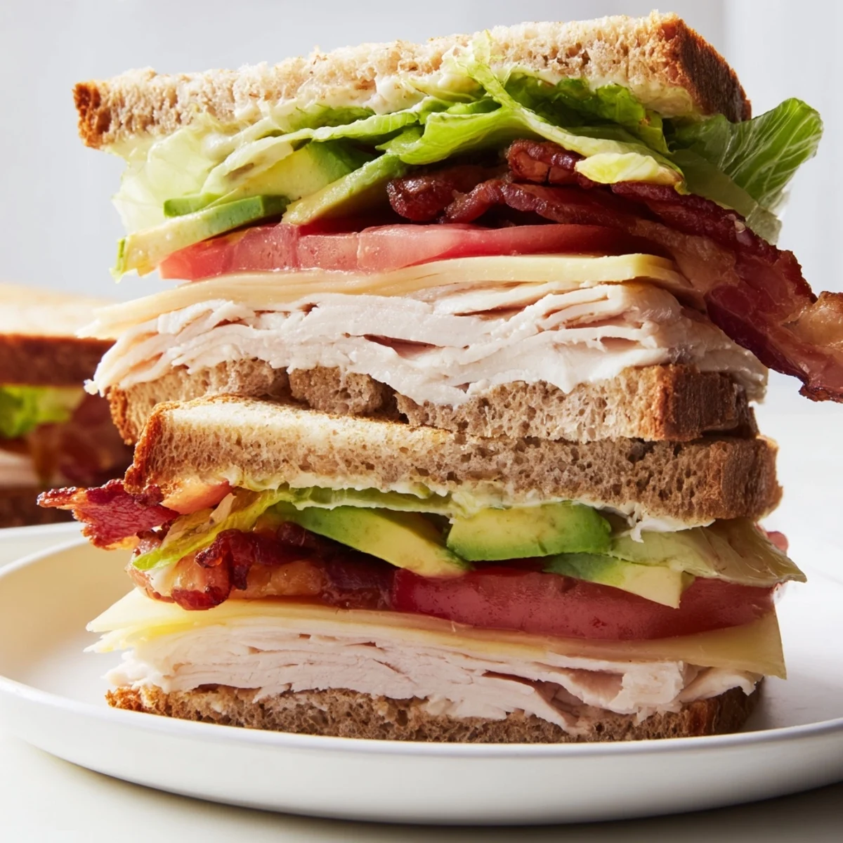 Fresh lettuce, tomato, and creamy avocado peek from the stacked Turkey Club Sandwich with Turkey Bacon served on a plate.