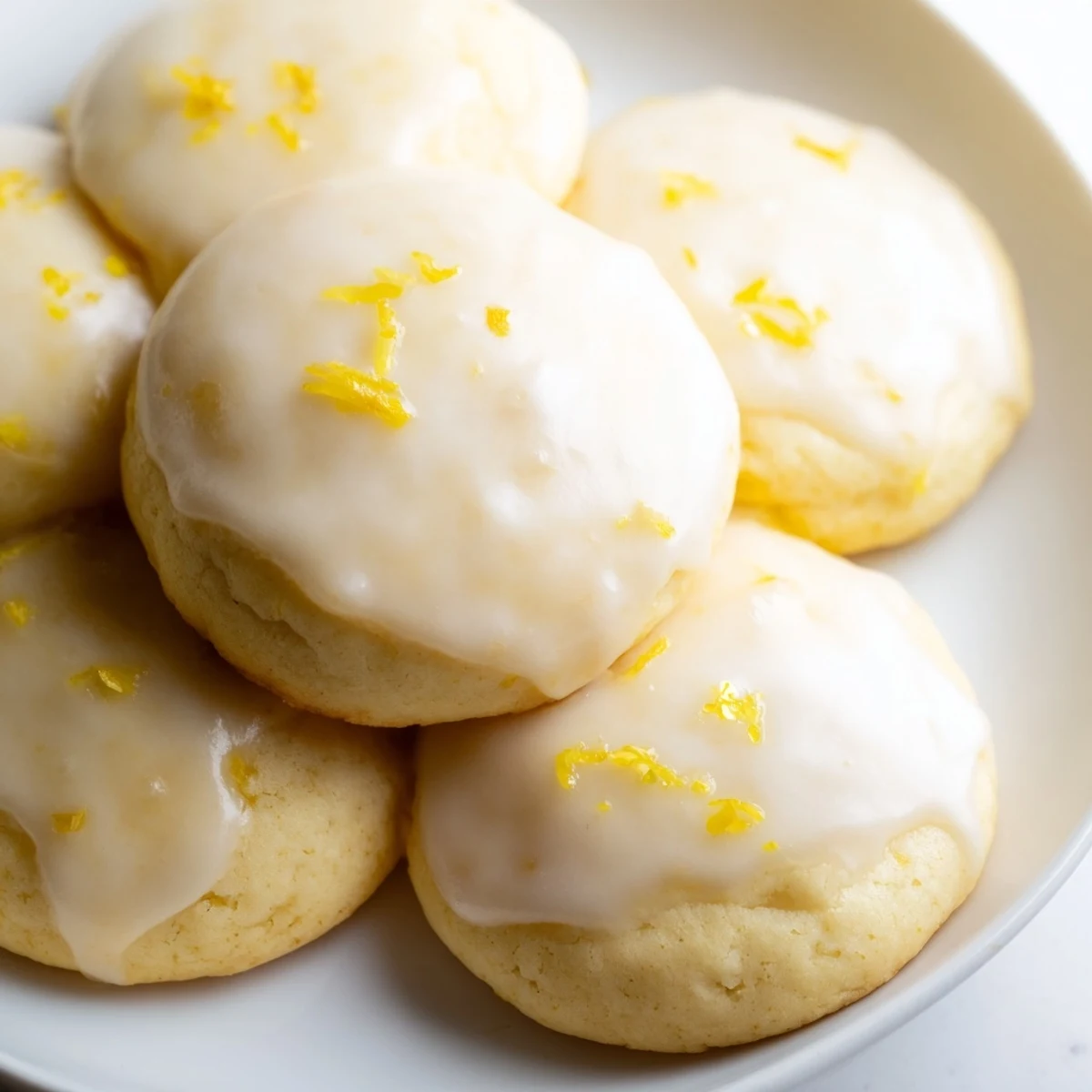 Lemon Ricotta Cookies with Glaze stacked on a white plate, glistening glaze catching light for a tempting treat.