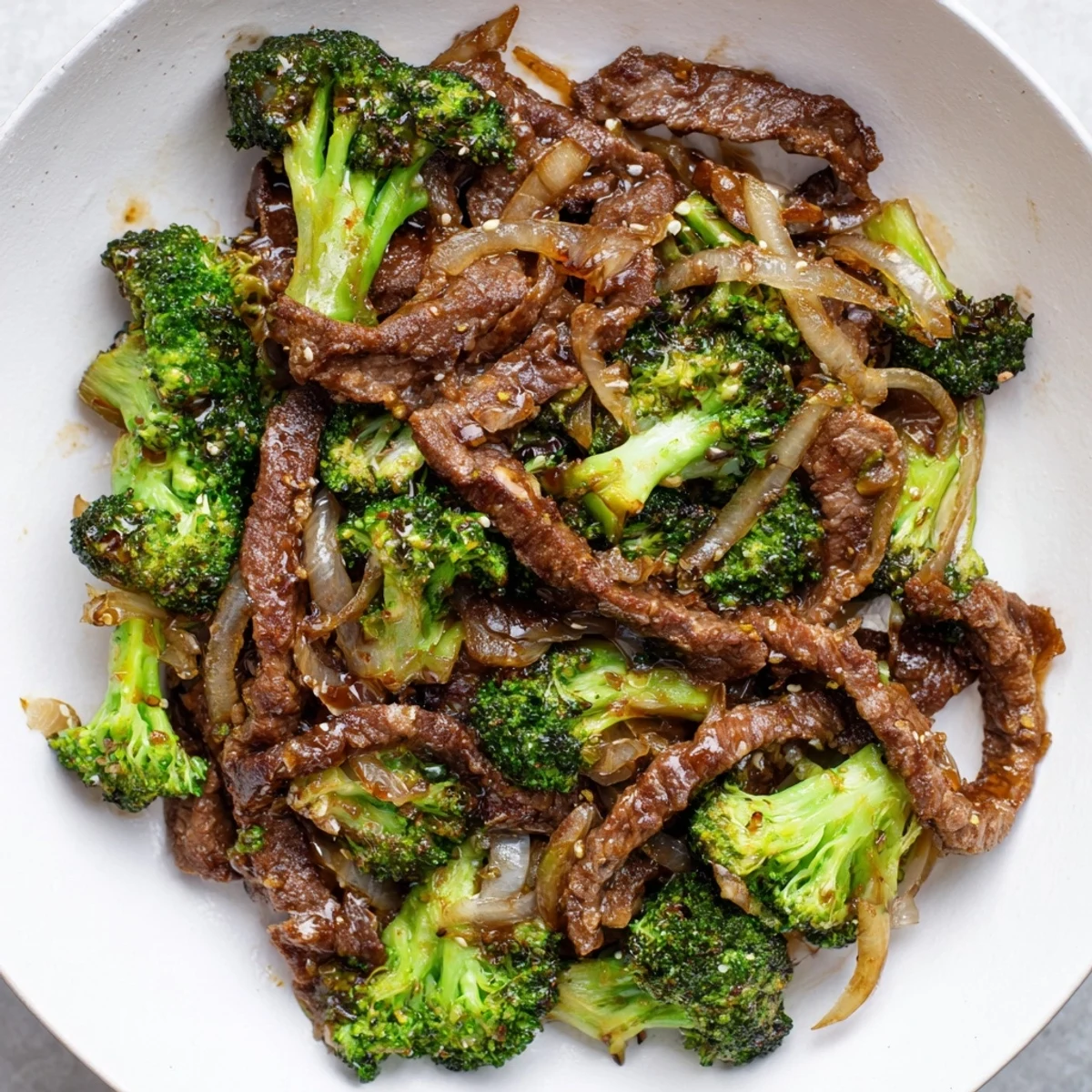 A close-up of Beef and Broccoli with Soy Sauce sizzling in a skillet, onions and sesame seeds adding texture and aroma.