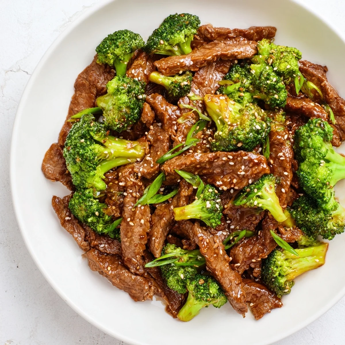 A close-up of a spoonful of Beef and Broccoli with Soy Sauce Glaze next to fluffy white rice and garnished with sesame seeds.