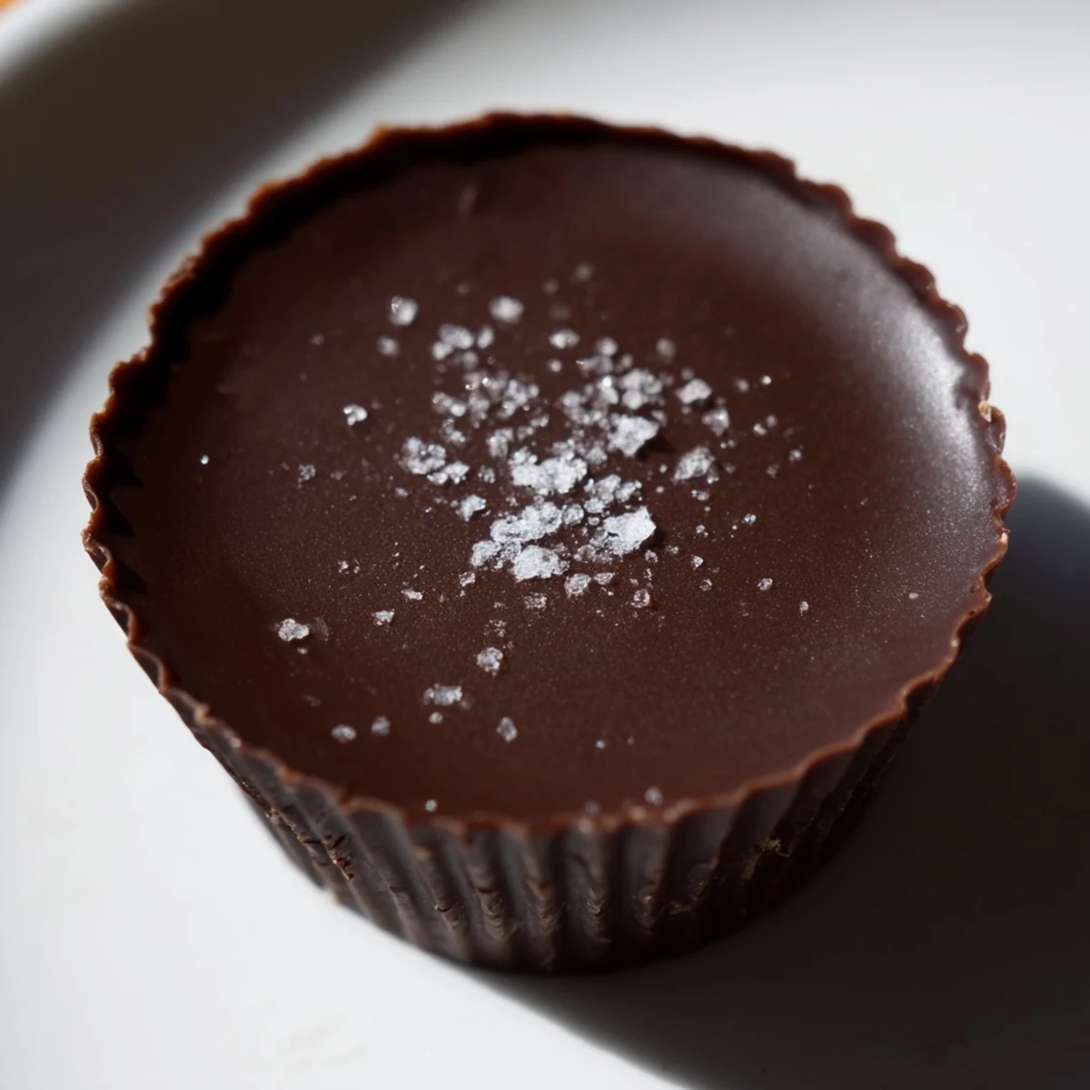 A close-up of homemade Chocolate Peanut Butter Cups glistening on a cooling rack with flaky sea salt.