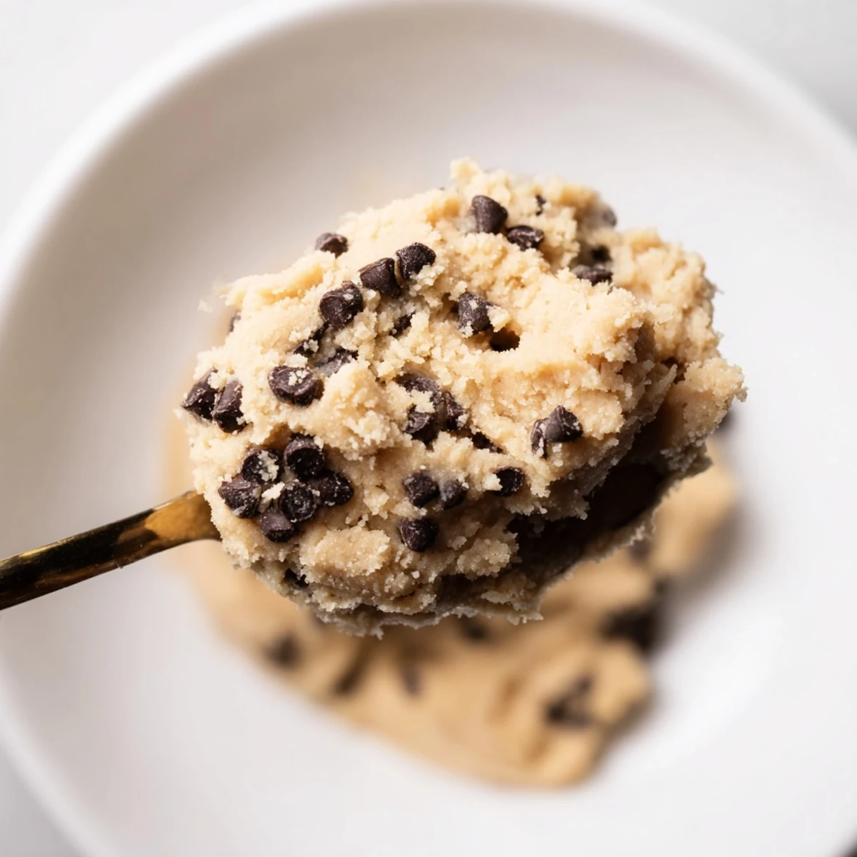 A spoon dipping into chilled Edible Keto Cookie Dough garnished with almond flour dust.