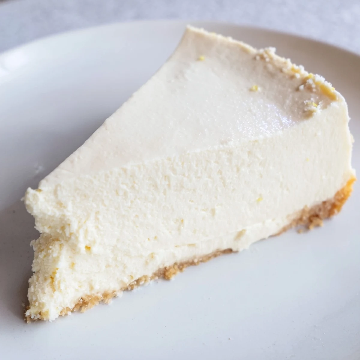 A slice of creamy Greek Yogurt Cheesecake with a golden graham cracker crust and tangy lemon zest.