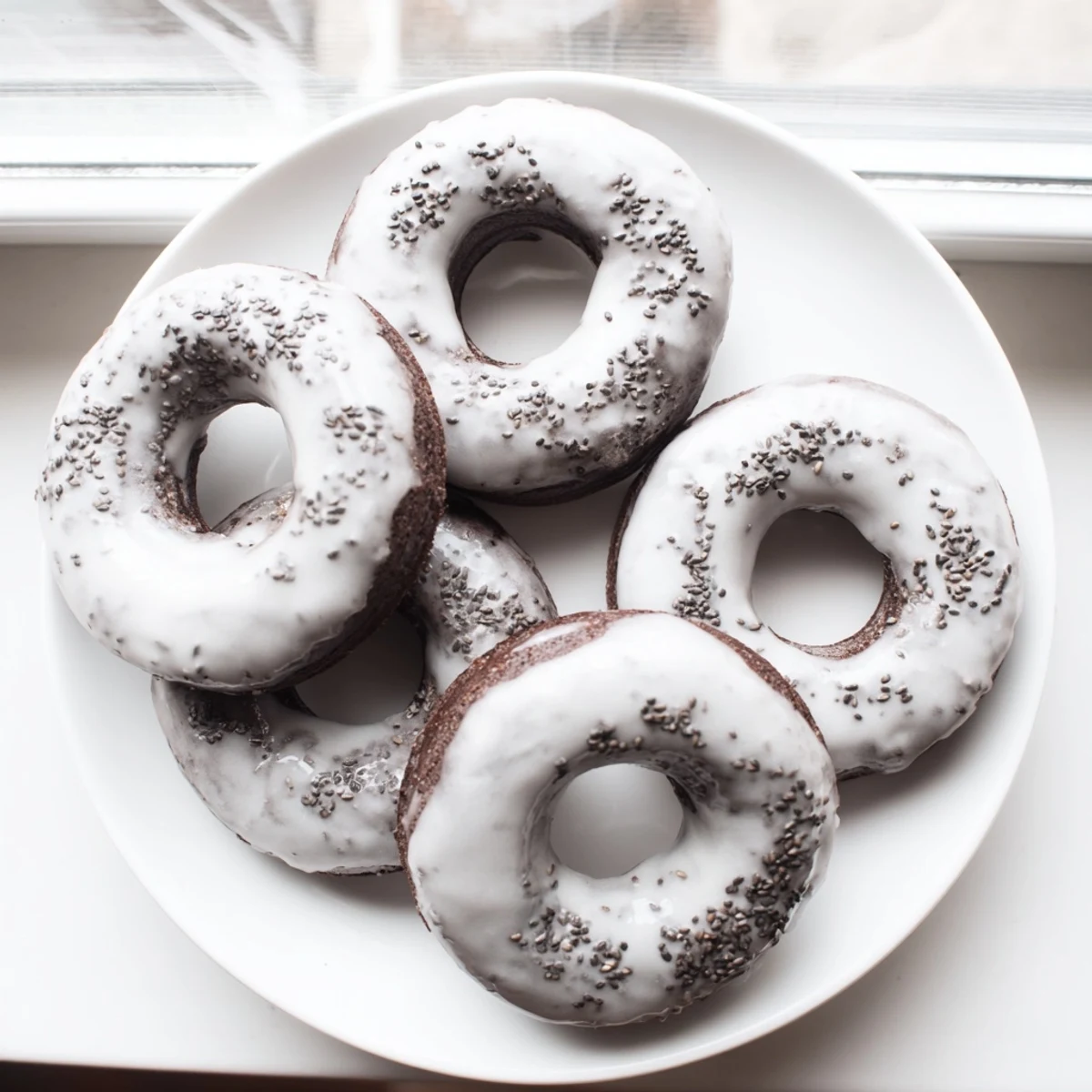 Twelve golden Black Sesame Mochi Donuts sit on a wire rack, glistening with a sweet glaze and sprinkled with sesame seeds.