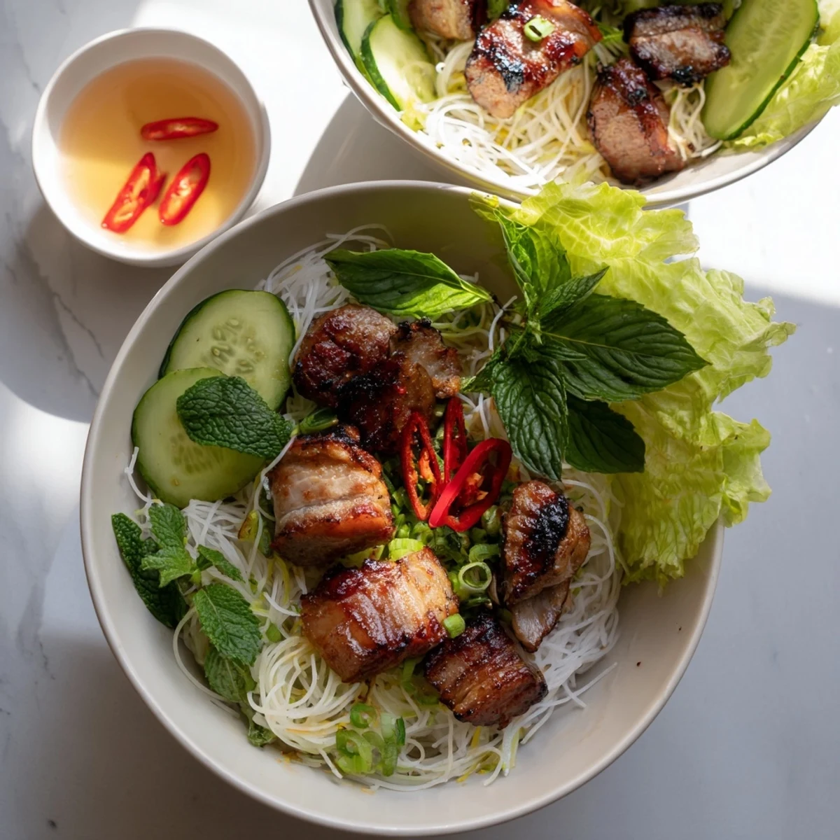 Sizzling Bun Cha Hanoi featuring caramelized pork patties and belly over noodles, garnished with cilantro, mint, bean sprouts, and a tangy nuoc cham sauce.