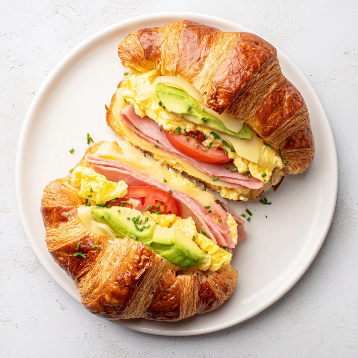 Flaky Croissant Breakfast Sandwich stacked high with melty cheese and savory ham on a plate. 