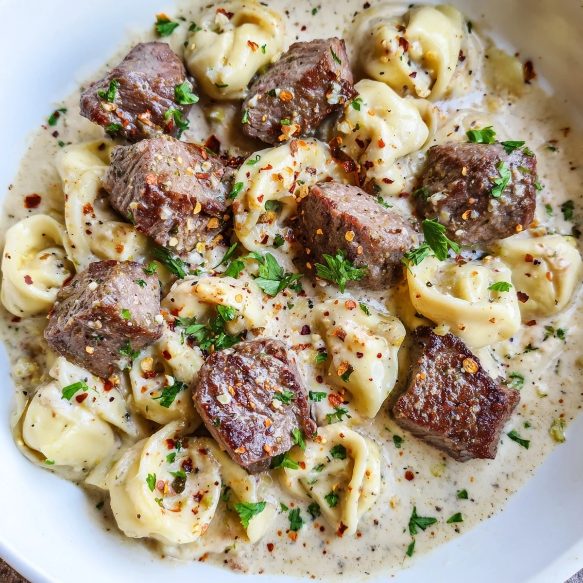 A close-up of Garlic Steak Tortellini in a creamy garlic sauce with tender steak pieces and fresh parsley garnish.