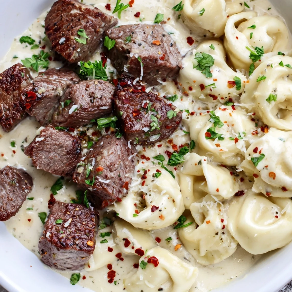Close view of Garlic Steak Tortellini topped with Parmesan and parsley, perfect for an easy Italian-American weeknight dinner.