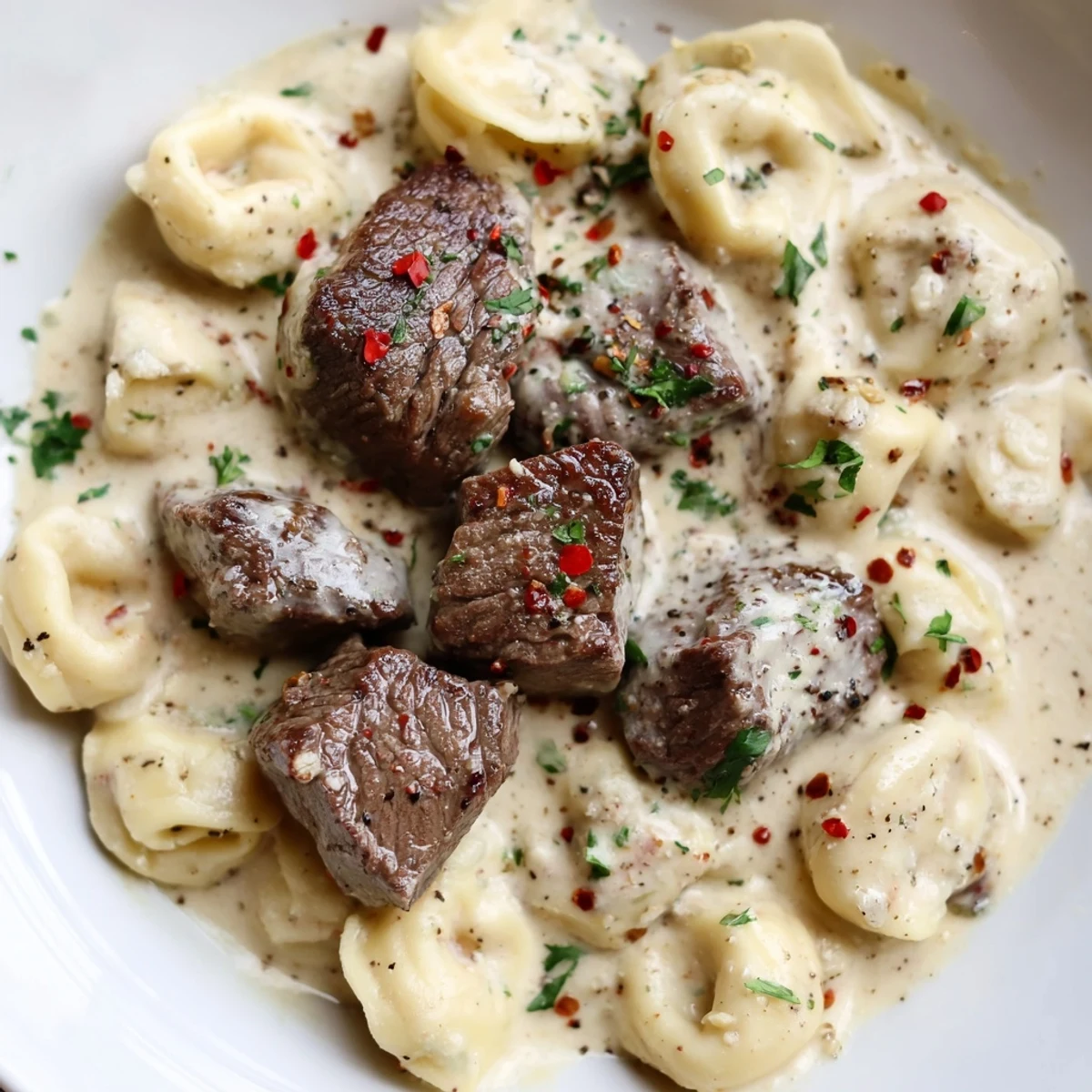 Steak and cheese tortellini tossed in a rich garlic cream sauce in a skillet, served as a decadent main dish.