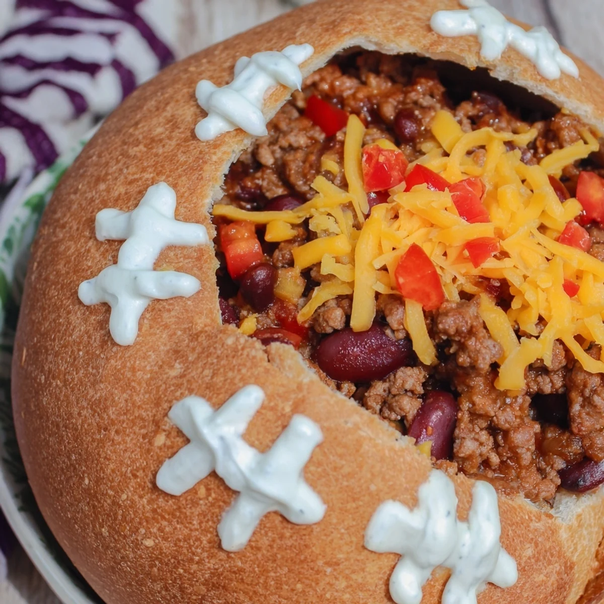 Hot Mini Chili Football Bread Bowls with melted cheddar, sour cream laces, and fresh green onion garnish on a game day platter.