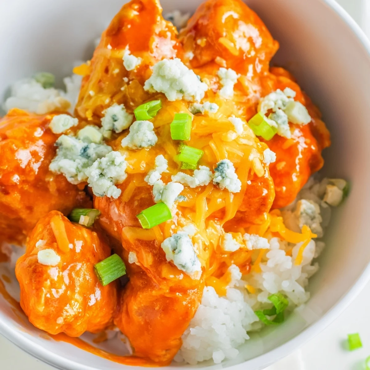 Freshly cooked spicy buffalo chicken pieces glisten with tangy sauce beside fluffy white rice and crisp toppings in a vibrant bowl. Buffalo Chicken Bowls recipe