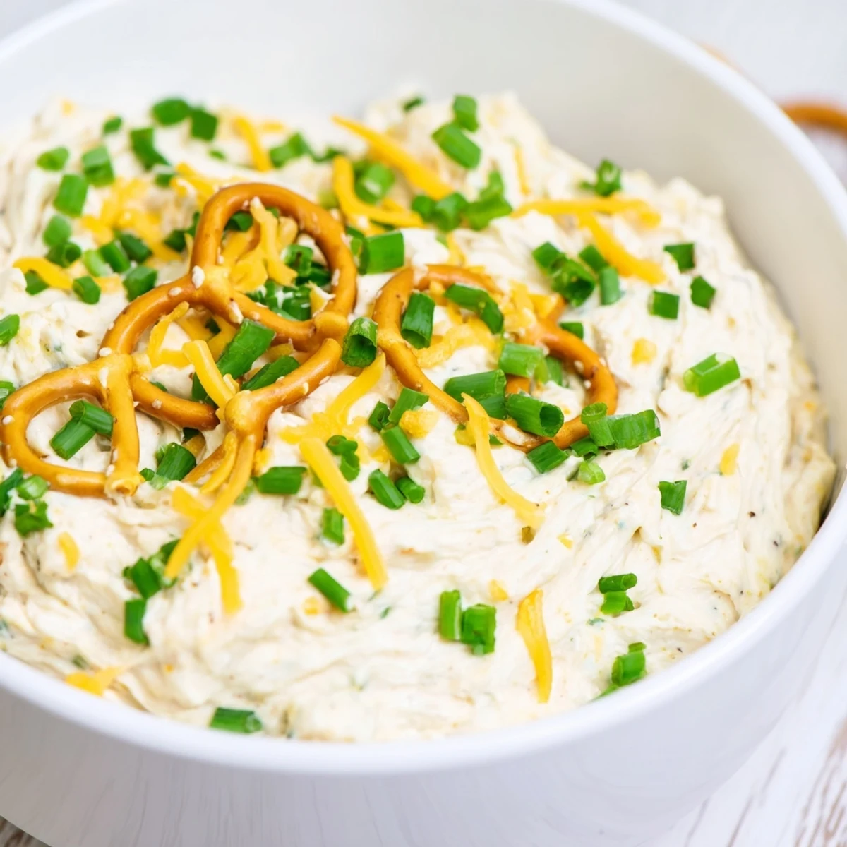 Creamy savory pretzel dip with melted cheddar and fresh chives served in a white bowl
