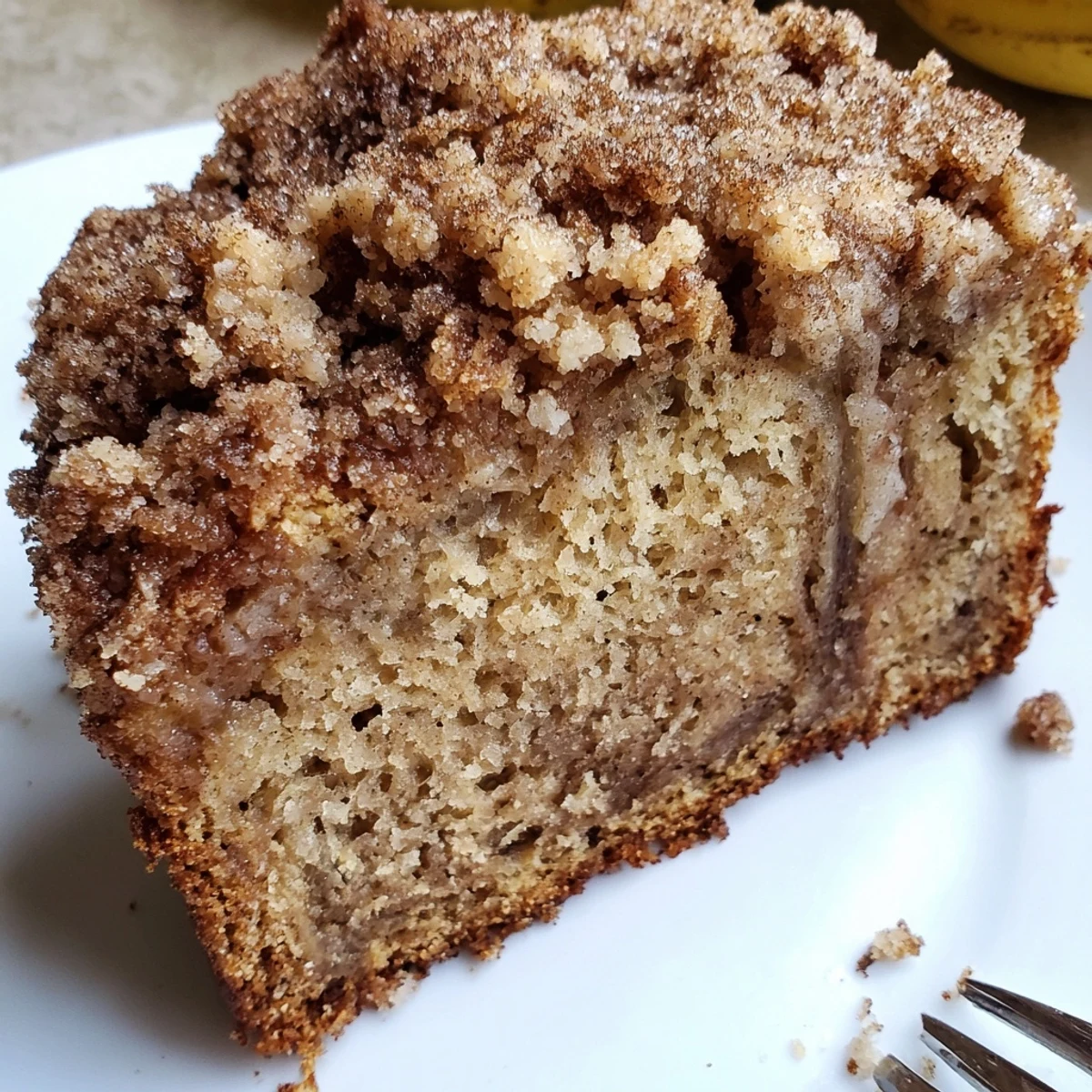 Warm slice of cinnamon crumb banana bread served on a white plate with melting butter