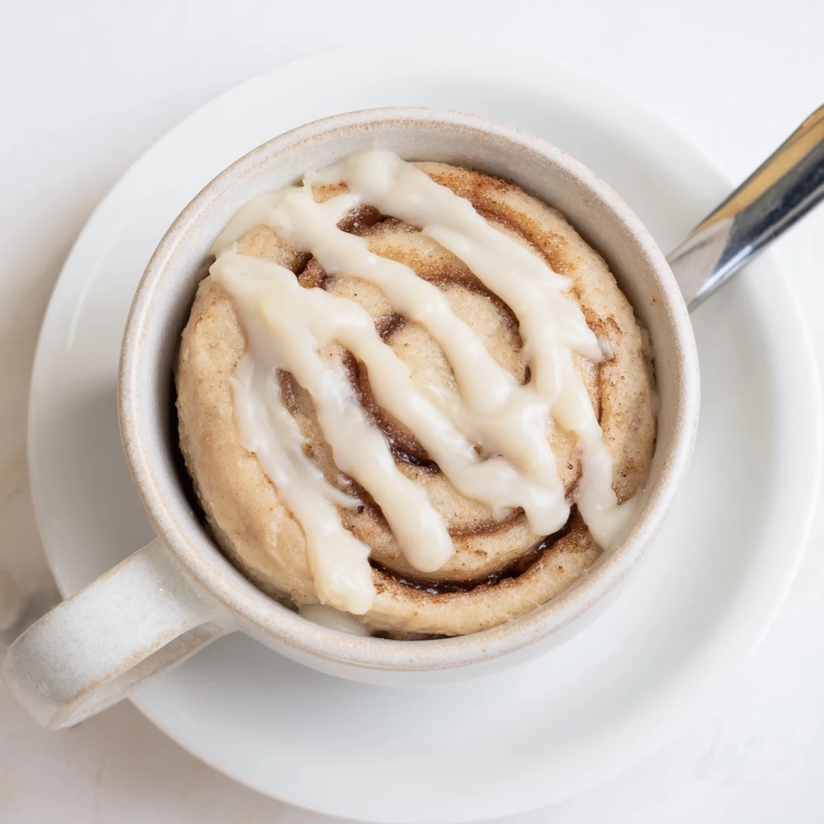 Single-serve protein-packed cinnamon roll mug cake with melting icing, served warm on a dark surface