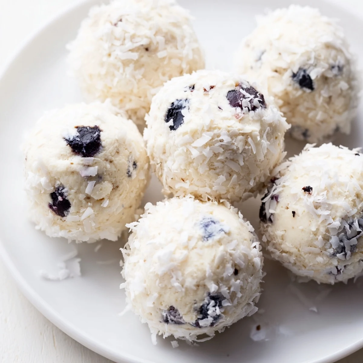 Creamy blueberry cheesecake protein bites arranged on a white plate, topped with fresh blueberries and coconut coating