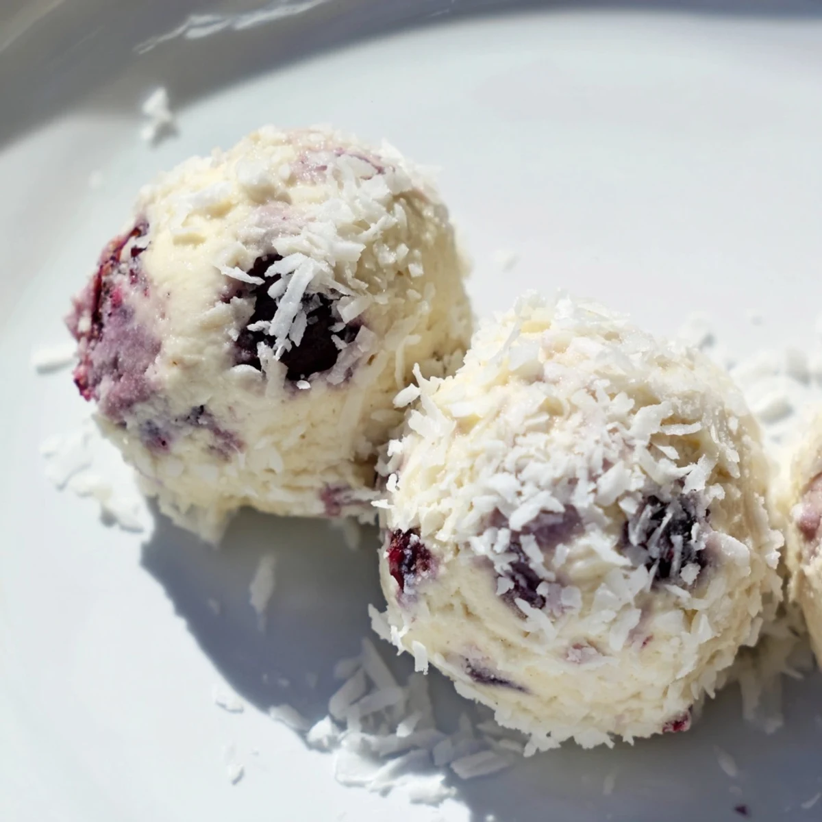 Close-up of protein-rich blueberry cheesecake balls rolled in shredded coconut, bursting with purple fruit pieces