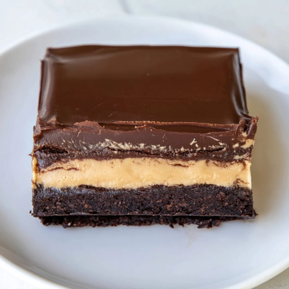 Homemade layered peanut butter brownies with smooth chocolate ganache drizzle served on white dessert plate