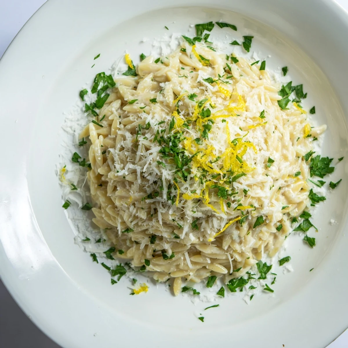 Creamy lemon orzo pasta with fresh parsley and grated Parmesan cheese in a white serving bowl
