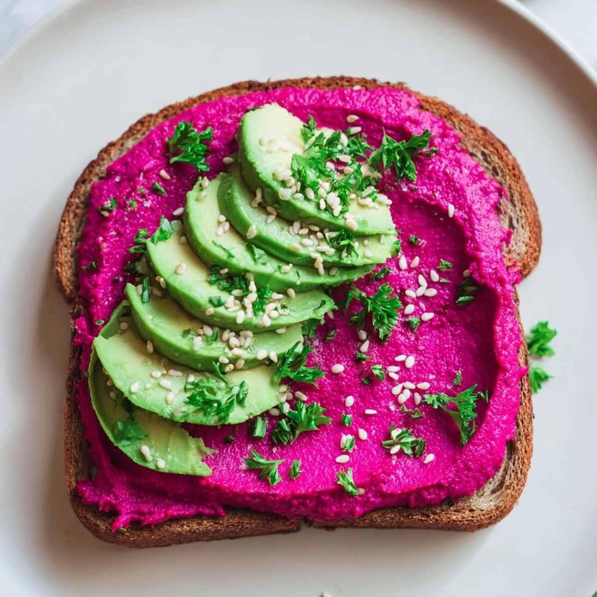 Colorful avocado beet hummus toast showcasing bright pink spread against toasted whole grain bread with sliced avocado and seed topping