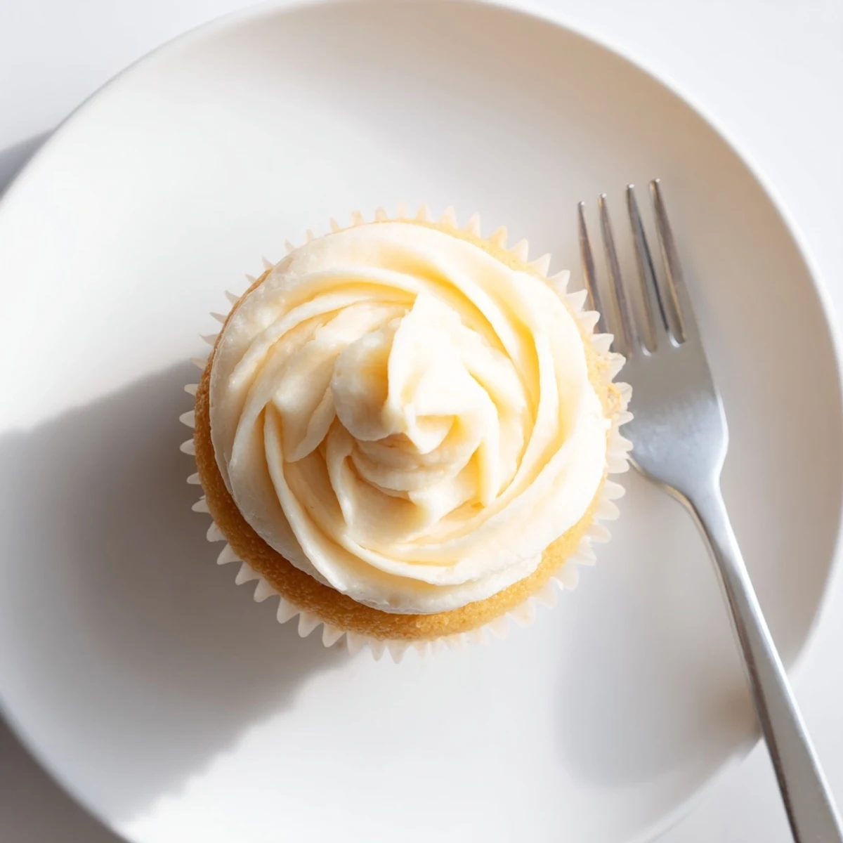 Light and fluffy vanilla cupcakes decorated with swirls of creamy white frosting on white plate