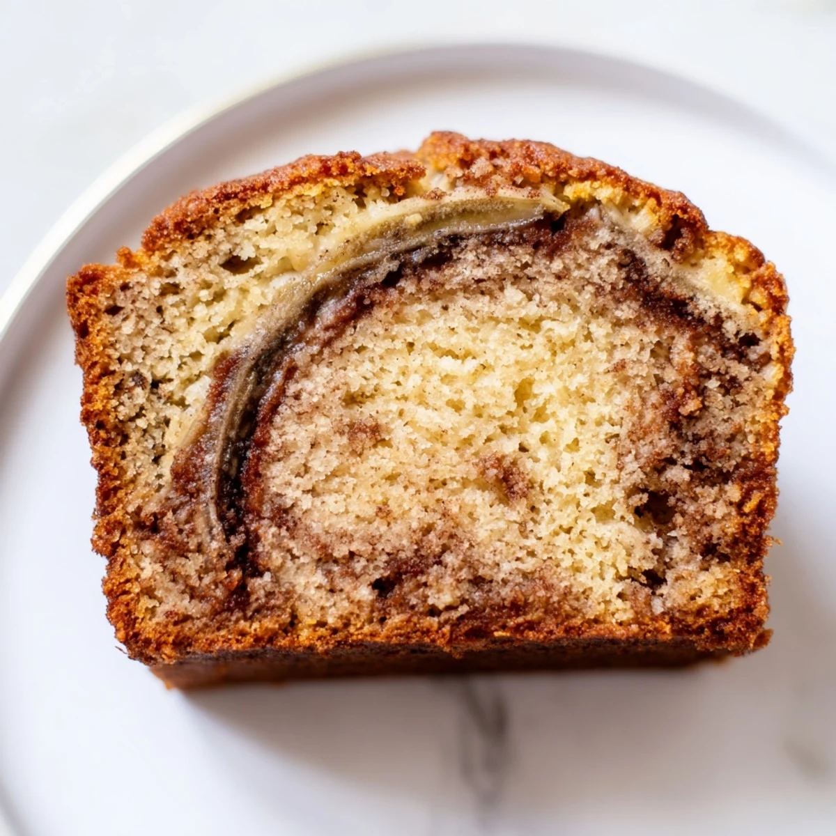 Moist cinnamon sugar swirl banana bread sliced thick on a wooden cutting board with crumbs