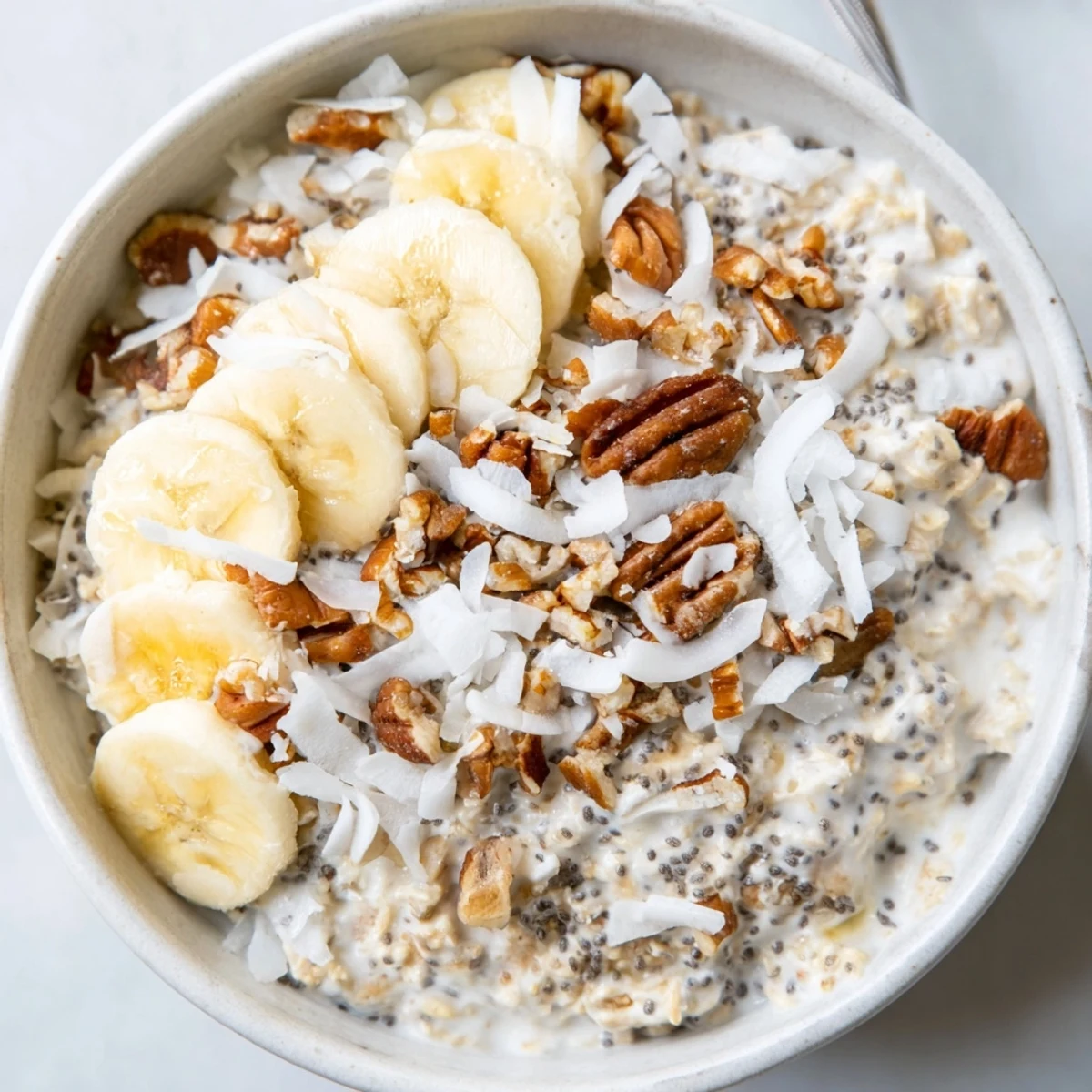 Coconut cream pie overnight oats layered in a jar with crunchy pecan topping