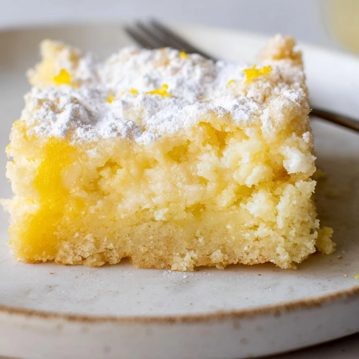 Golden Lemon Gooey Butter Cake squares dusted with powdered sugar on a rustic serving plate