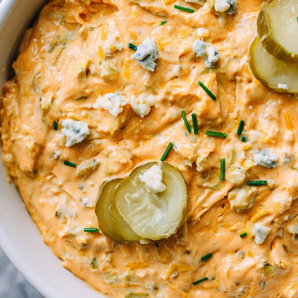 Creamy buffalo pickle dip in a serving bowl surrounded by crunchy chips and fresh veggie sticks