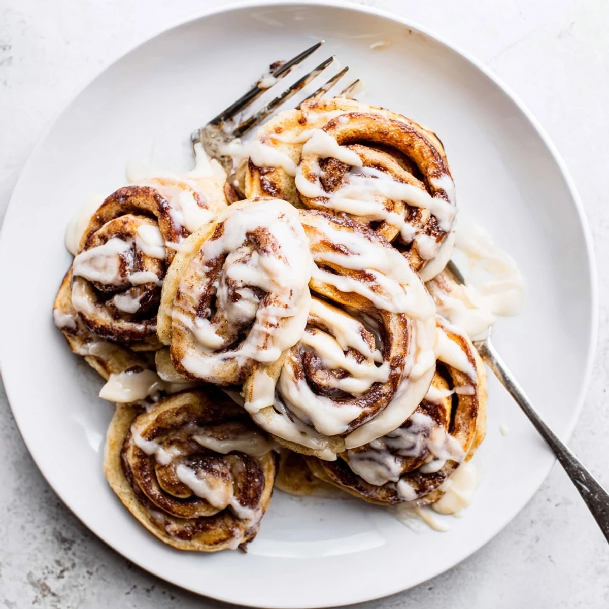 A stack of warm cinnamon roll pancakes drizzled with sweet cream cheese glaze