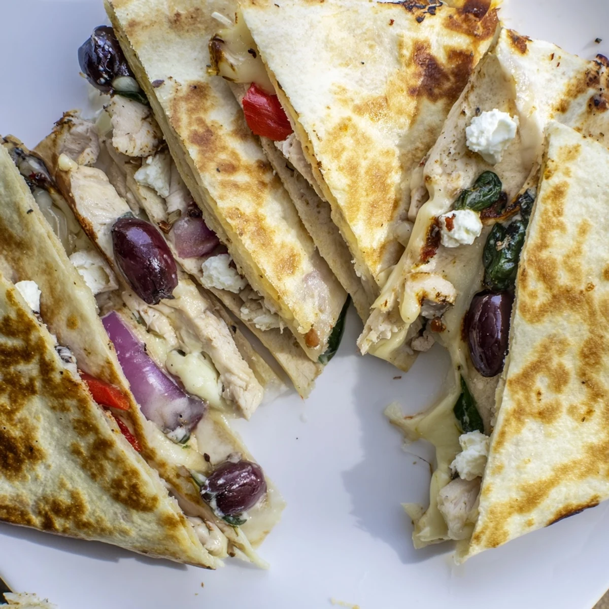 Homemade Greek chicken quesadillas sliced into wedges revealing juicy meat and gooey cheese filling
