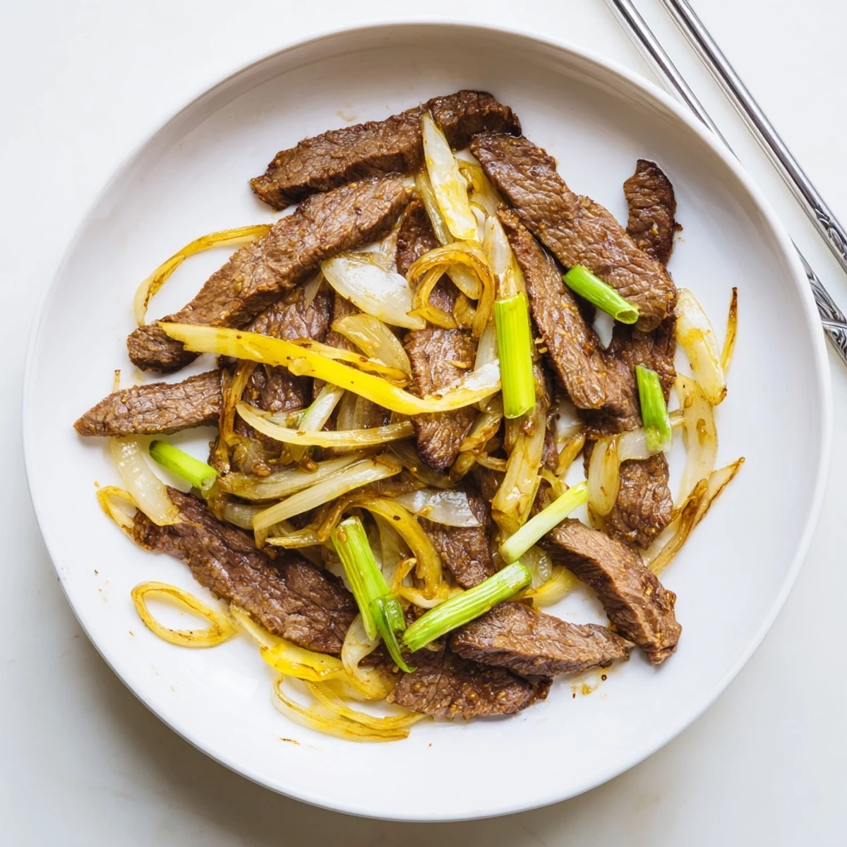 Golden brown crispy beef and onion stir fry served in a white bowl over steaming jasmine rice