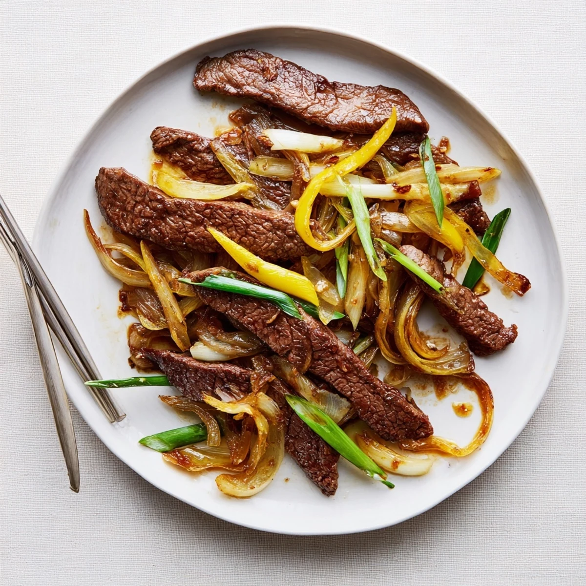 Tender slices of caramelized beef and sweet onions coated in glossy brown sauce on a wooden dining table