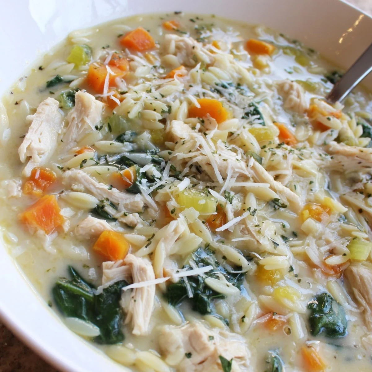 Bowl of Creamy Chicken Florentine Soup With Orzo, wilted spinach, Parmesan.