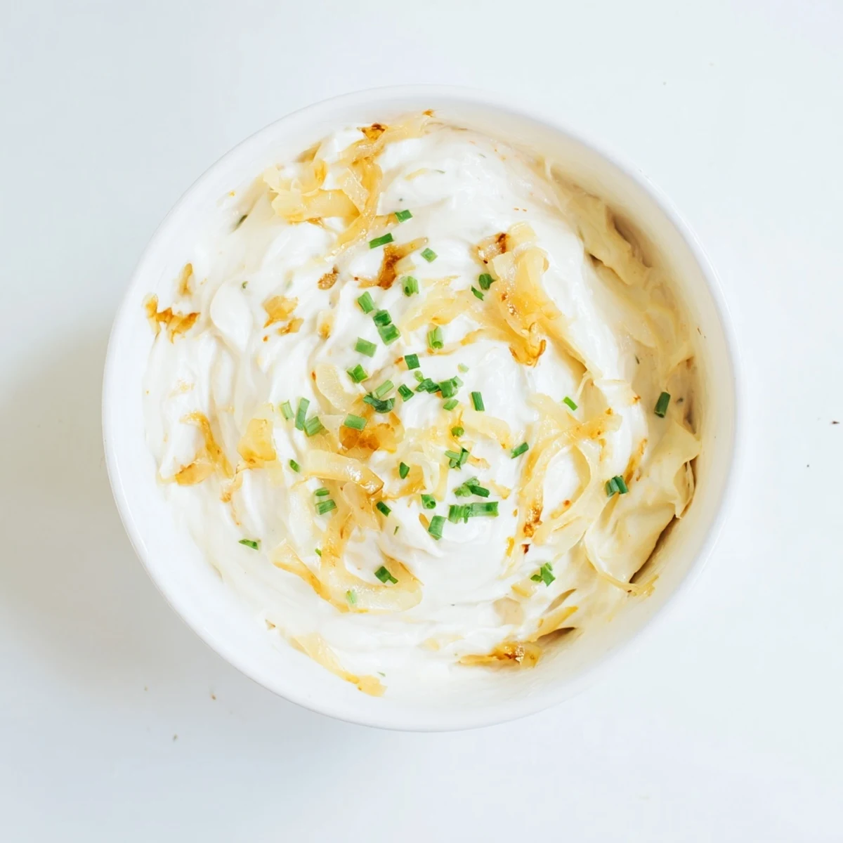 Creamy French onion dip topped with caramelized onions and fresh chives served in a white bowl