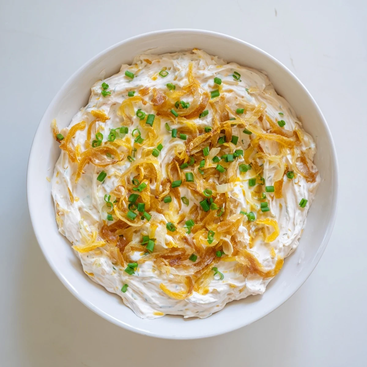 Bowl of savory French onion dip with sweet melted onions and a sprinkle of fresh herbs
