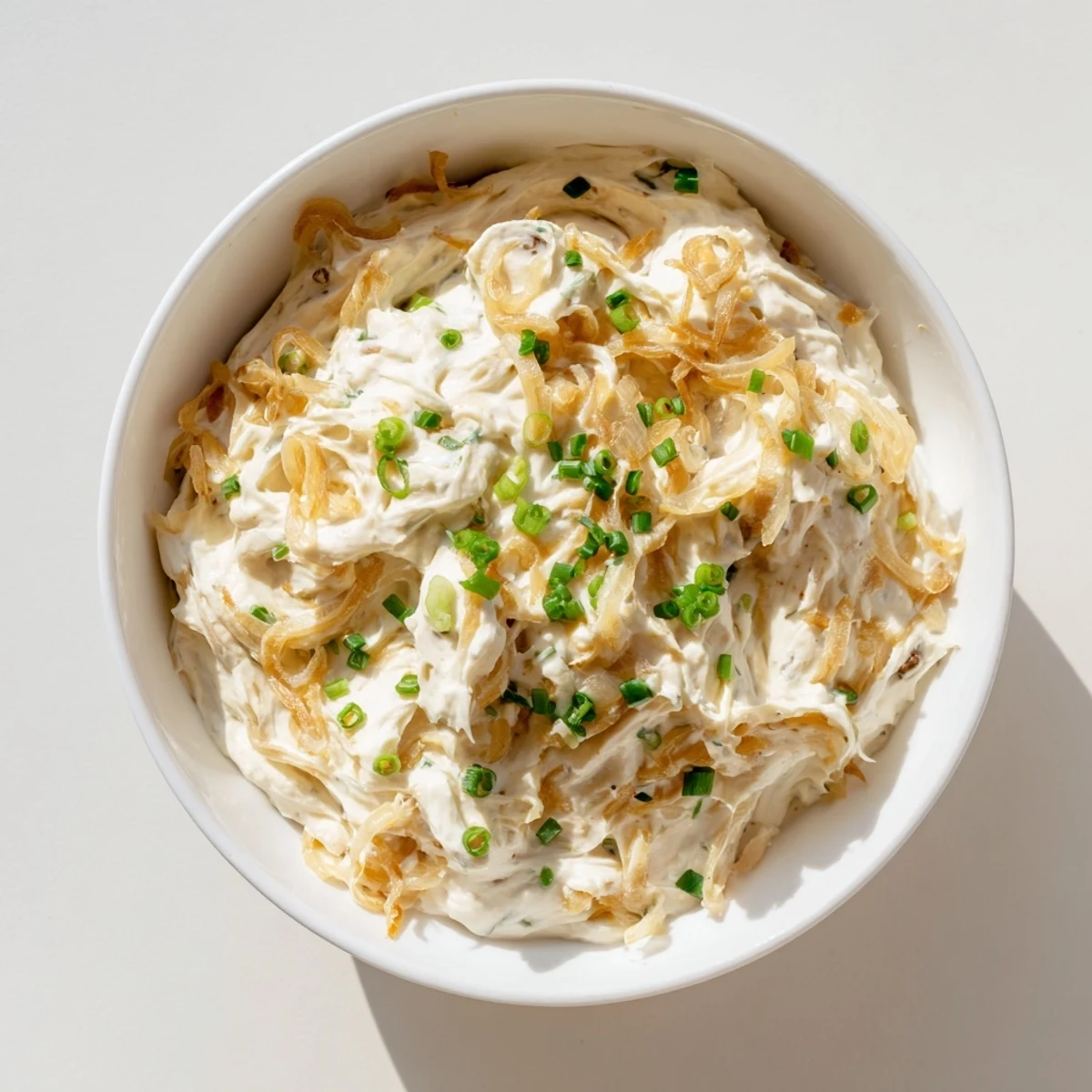 Rich homemade French onion dip with golden brown caramelized onions garnished with green onion pieces