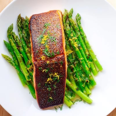 Perfectly cooked Pan Seared Salmon with Asparagus Spears plated on white ceramic, featuring crispy skin, tender green spears, and a drizzle of lemon butter sauce.