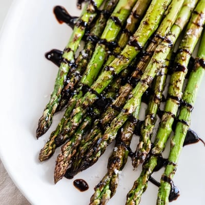 Roasted asparagus with balsamic glaze drizzled over spears, served warm as a vegetable side.