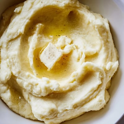 Creamy Velvety Mashed Potatoes cascading from a spoon onto a festive holiday dinner plate