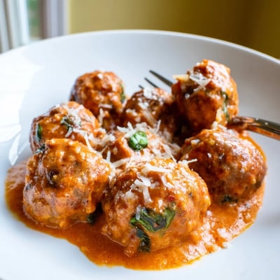 Steaming skillet of Creamy Tomato Basil Meatballs swimming in rich, red parmesan-tinted tomato basil sauce